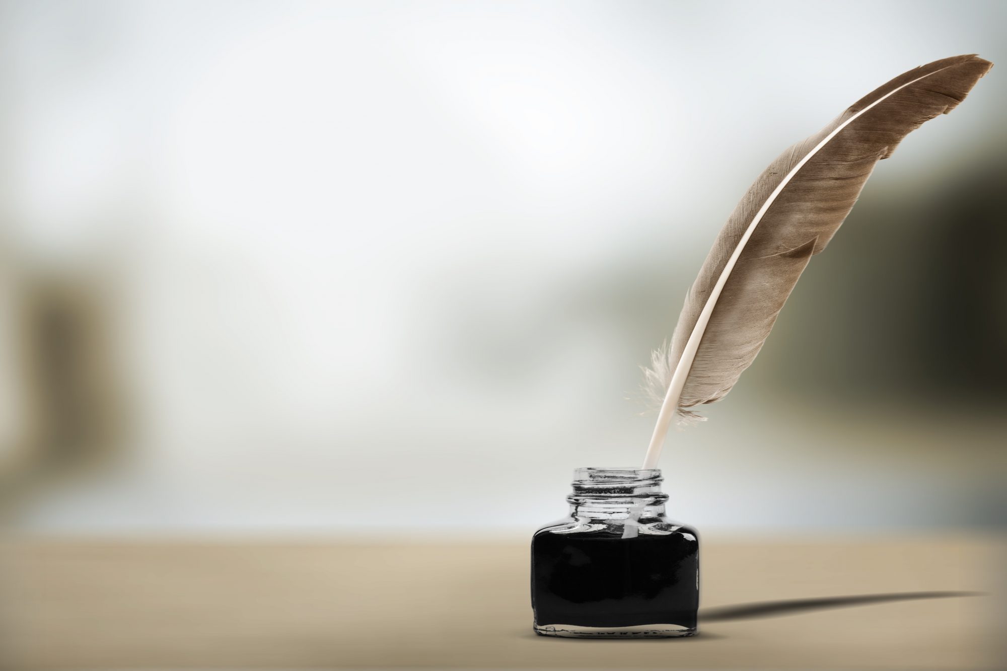 Eine braune Feder steckt in einem Glas-Tintenfass auf hellem Untergrund – ein Symbol für Schreiben, Gedankenfluss, Reflexion und Inspiration.