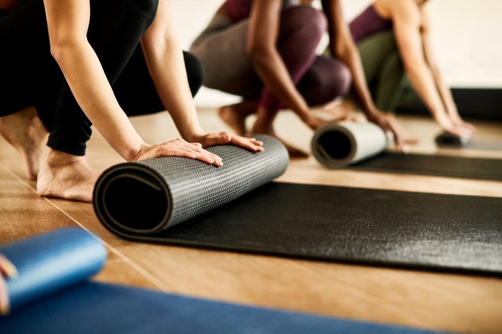 Mehrere Menschen rollen im Yogaraum ihre Matte aus – bereit für den Kursbeginn. Ein Moment des Ankommens, der Konzentration und des gemeinsamen Starts.