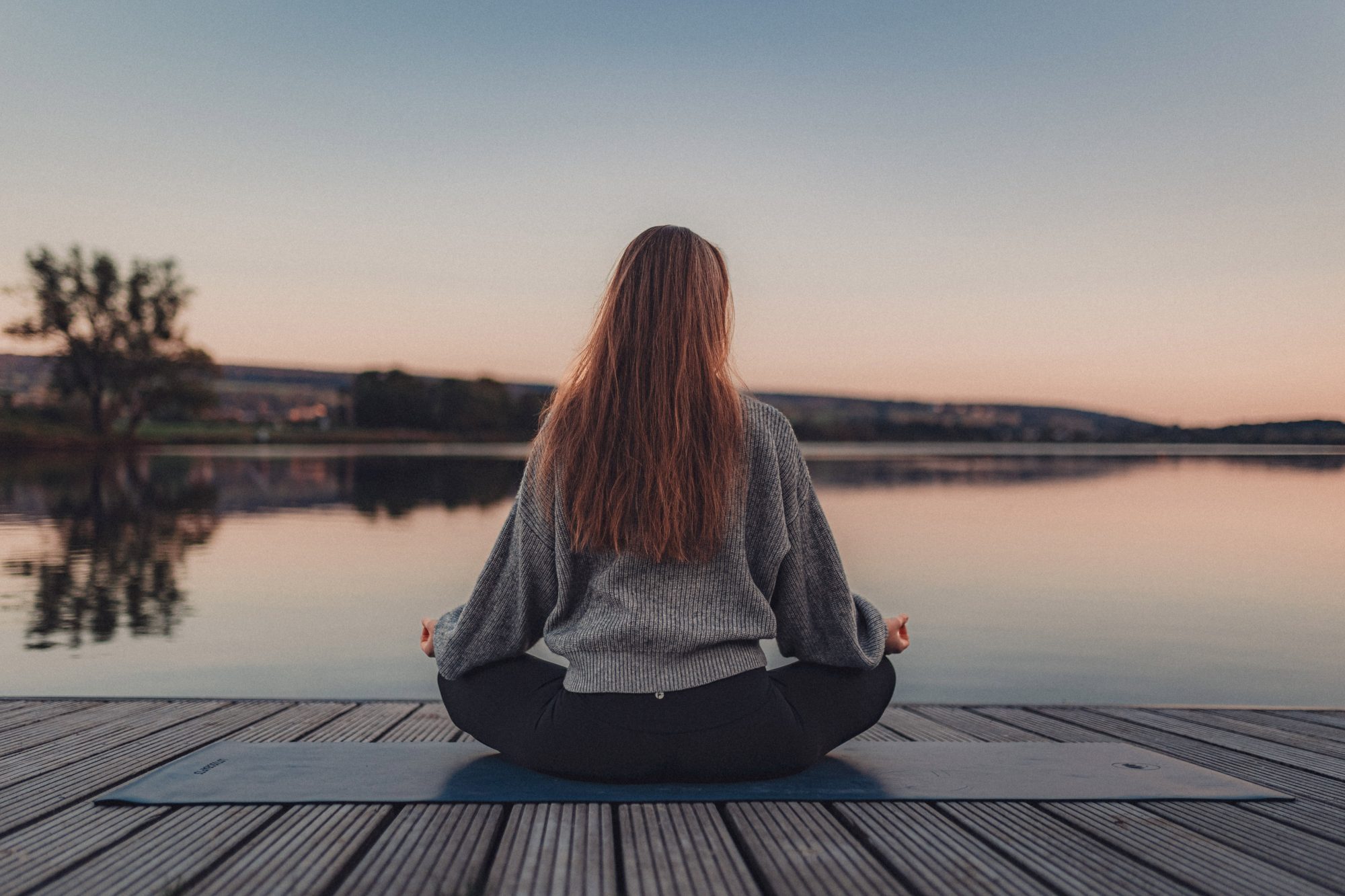 Yogalehrerin Helena Gnaase sitzt in Meditation auf einer Yogamatte vor einem stillen See – Sinnbild für Yin Yoga, Ruhe und innere Klarheit.