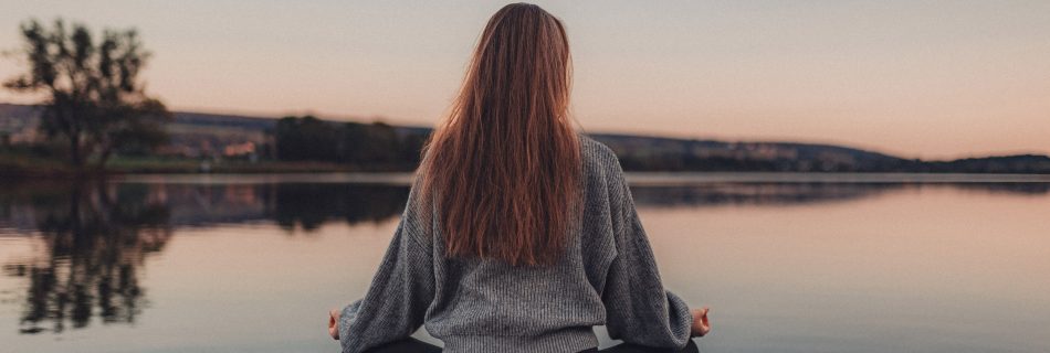 Yogalehrerin Helena Gnaase sitzt in Meditation auf einer Yogamatte vor einem stillen See – Sinnbild für Yin Yoga, Ruhe und innere Klarheit.